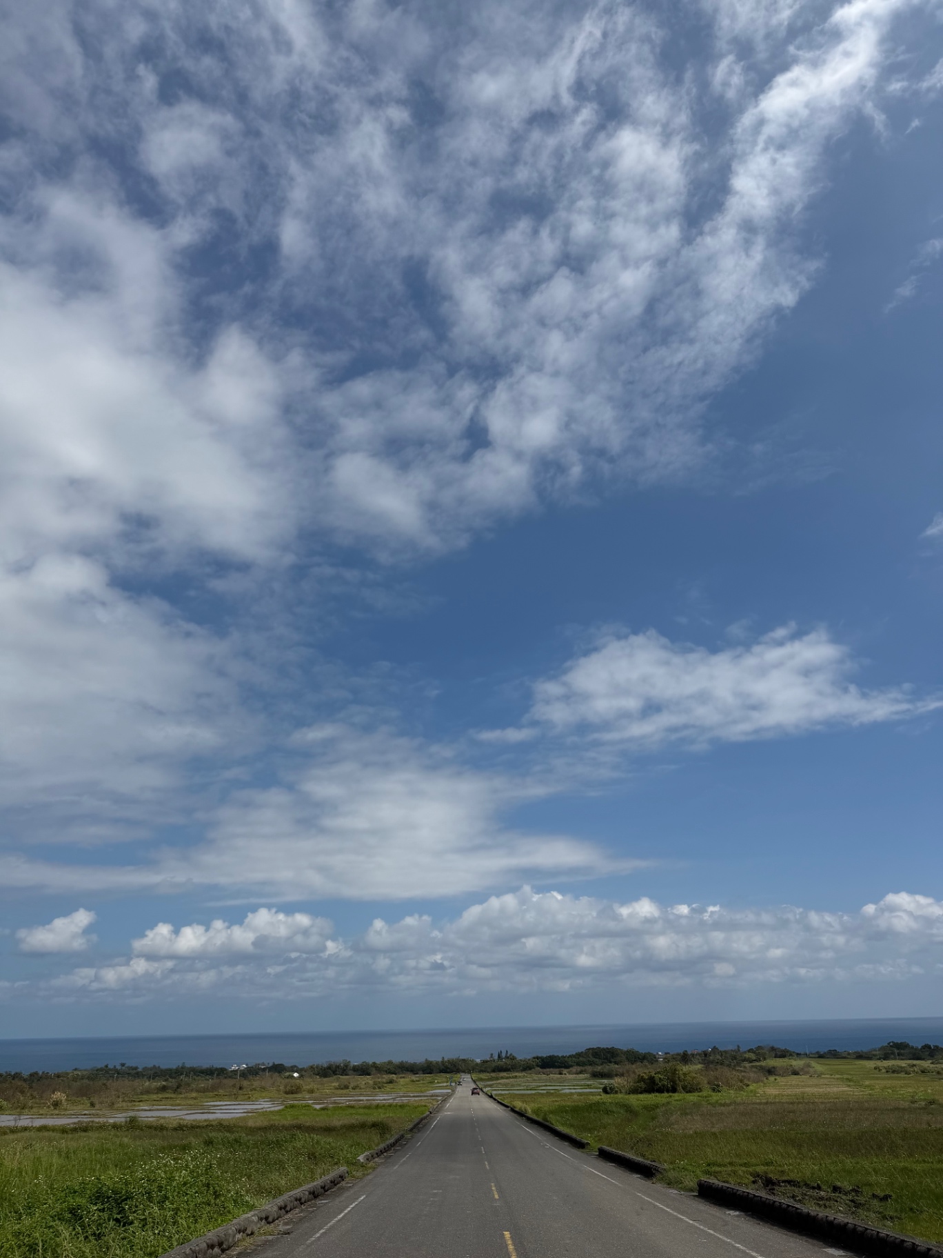 Empty coastal highway running straight toward the Pacific under wide clouds