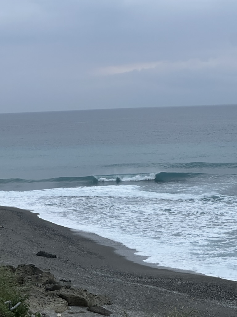 Peeling wave breaking along a dark sand and pebble beach