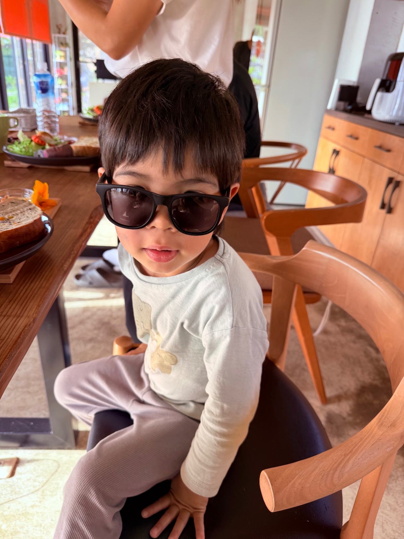 Kid in shades at a sunlit breakfast table